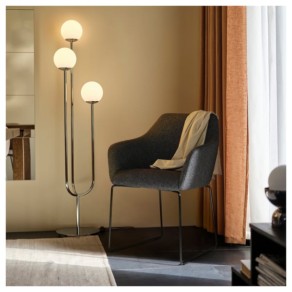 Moderní jídelní kout: šedá židle TOSSBERG, béžová deka, elegantní stojací lampa se třemi zářícími koulemi.