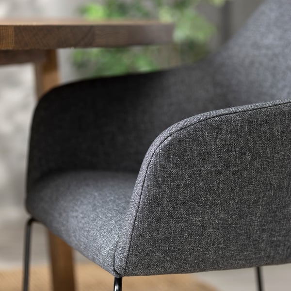 Detailní záběr na moderní šedé látkové křeslo s elegantními područkami a kovovými nohami.