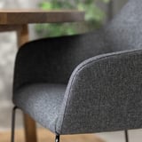 Detailní záběr na moderní šedé látkové křeslo s elegantními područkami a kovovými nohami.