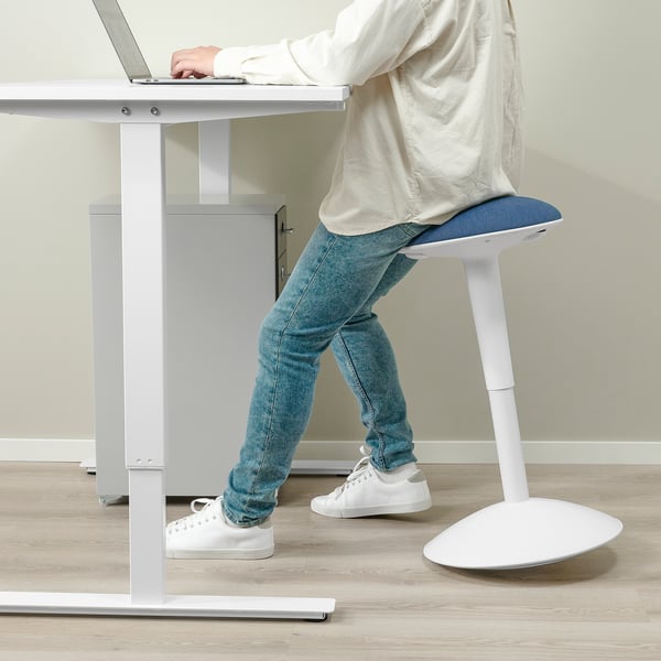 Osoba sedící u výškově nastavitelného stolu na ergonomické stoličce, píšící na notebooku.