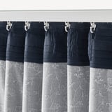 Tmavě modré závěsy s bílými květinovými vzory úhledně visí ze stříbrných spon. Design filtruje světlo a nabízí soukromí.