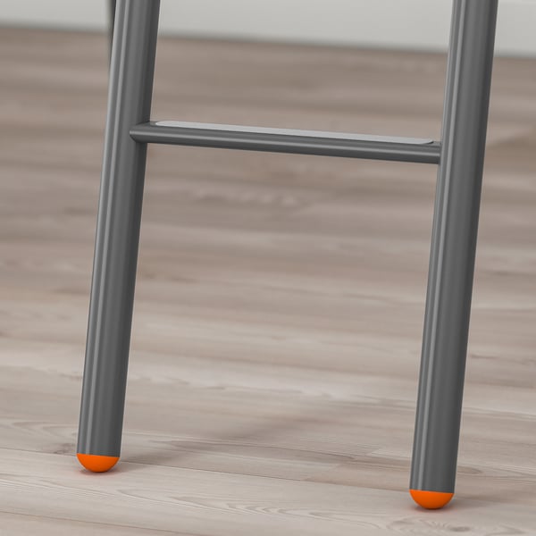Detail kovových nohou patrové postele s oranžovými špičkami pro stabilitu na dřevěné podlaze.