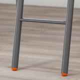 Detail kovových nohou patrové postele s oranžovými špičkami pro stabilitu na dřevěné podlaze.