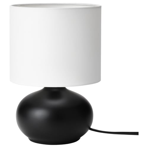 Moderní stolní lampa, TVÄRFOT. Černá, oválná kameninová základna. Bílý válcový odstín. Jednoduchý, stylový design.
