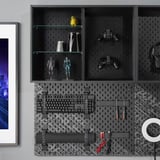 Černá pegboard UPPSPEL s příslušenstvím: dva herní ovladače, figurky, klávesnice, sluchátka, nářadí a kabely úhledně uspořádané.