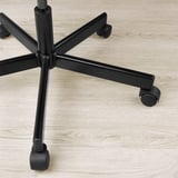 Detail základny židle s robustními, nastavitelnými kolečky na podlaze ze světlého dřeva.