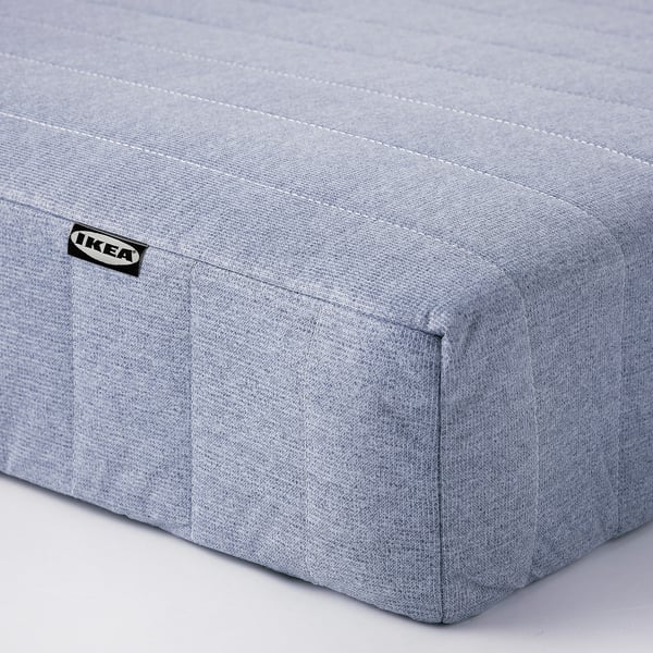 Ukazuje jednoduchou, světle šedou matraci IKEA s minimalistickým designem a viditelným prošíváním, což svědčí o kvalitní konstrukci.