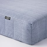 Ukazuje jednoduchou, světle šedou matraci IKEA s minimalistickým designem a viditelným prošíváním, což svědčí o kvalitní konstrukci.
