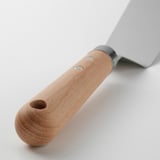 Detailní záběr špachtle s rukojetí z bukového dřeva a čepelí z nerezové oceli, která ukazuje její robustní design a otvor pro zavěšení pro snadné skladování.