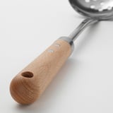 Předradlík s dřevěnou rukojetí a kovovou miskou navržený pro snadné zavěšení a bezpečné uchopení.