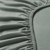 Detailní záběr z měkkého zeleného žerzejového materiálu s elastickým okrajem, který předvádí kvalitní texturu a prošívání.
