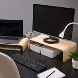 Dřevěný stojan na monitor s notebookem, úložištěm klávesnice, na tmavém stole. Obsahuje lampu, rostlinu, bezdrátovou klávesnici a poznámkový blok pro efektivní pracovní prostředí.