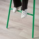 Nohy osob s ponožkami se srdcovým vzorem spočívají na zelených nohách dětské židle, což předvádí její design opěrky nohou pro děti.
