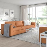 Moderní obývací pokoj s oranžovou pohovkou VIMLE, mix kůže a látky. Přirozené světlo naplňuje minimalistický prostor bílým dekorem.