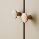 Dva hladké dřevěné knoflíky světlé barvy namontované na béžové skříni, které předvádějí elegantní a jednoduchý design.