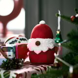 Sedící červená figurka Santy poblíž dárků. Menší než dárky.