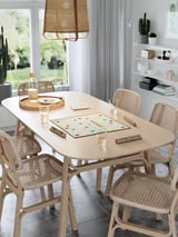 Moderní jídelní set se scrabble boardem, světlé dřevo, proutěné židle, přirozené světlo.