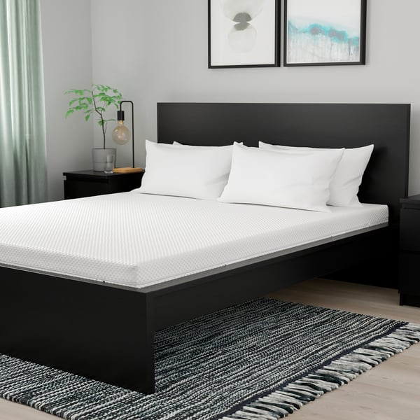 ÅBYGDA black foam mattress against white wall, with pillows, rug, plant, lamp, natural light.