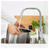 Person washing vegetables in kitchen sink with ÄLMAREN chrome tap, showcasing water efficiency and high spout functionality.