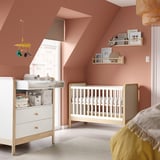 Modern nursery with white crib, changing table, pink walls, and hanging decor.