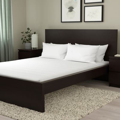 Modern bed with ÅFJÄLL foam mattress, dark wood frame, white spread, green walls, art prints, nightstand with plant.