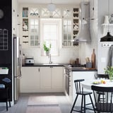 Modern kitchen with white cabinets, black chairs, stainless steel appliances, and a rug.