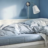 Bed with blue mattress, white sheets, wall lamp, blue wall.