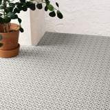 A tiled outdoor floor with triangular patterns, ideal for balconies. A potted plant sits on the left, highlighting its weather-resistant design.