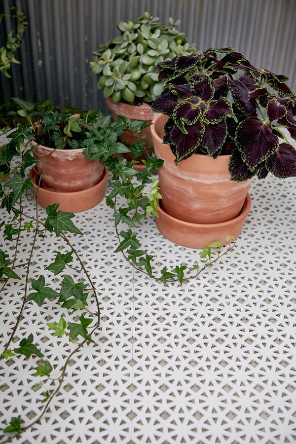 Three potted plants on white geometric-patterned ALTAPPEN floor decking, made of durable plastic, which is uv-stabilized and weather-resistant.