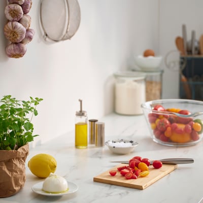 Modern kitchen counter with APTITLIG bamboo cutting board, sliced tomatoes, lemons, mozzarella, and kitchenware.