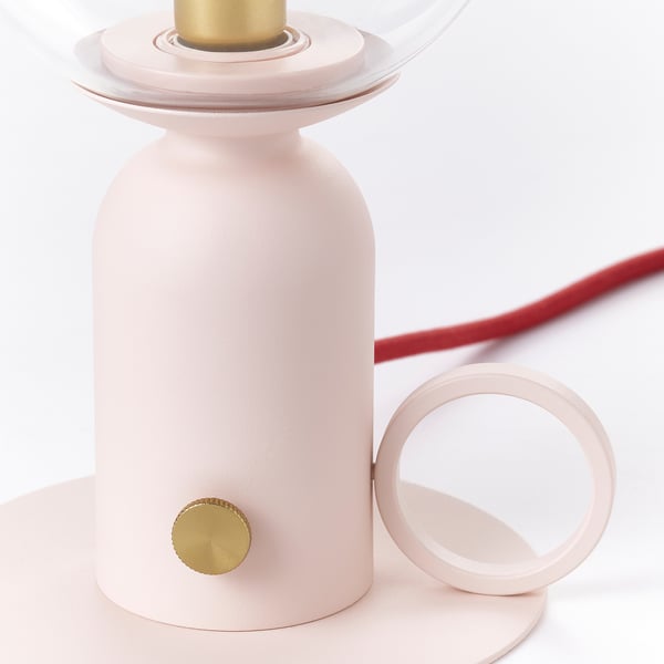 Modern pastel pink lamp with gold accents and red cord, displayed on light base.