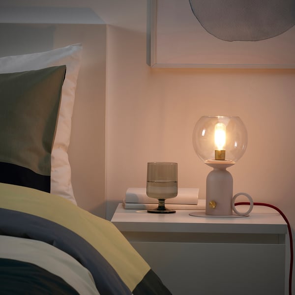 Cozy bedroom corner with white lamp, glass, book, colorful bedding. Or, for one word fewer: cozy bedroom nook: lamp, glass, book, colorful bed.