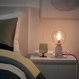 Cozy bedroom corner with white lamp, glass, book, colorful bedding. Or, for one word fewer: cozy bedroom nook: lamp, glass, book, colorful bed.