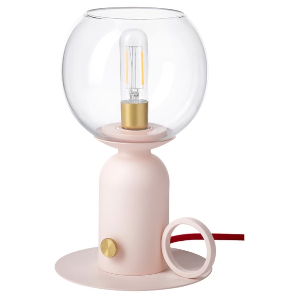 The ÅSKMULLER lamp is a sleek, modern table lamp in a light pink color with a rounded glass shade and gold accents, giving off a warm, cozy light.