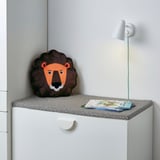 Soft lion pillow, book, and lamp on padded bench top.