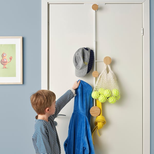 Child reaching for blue robe on adjustable BÄRFIS hanger, with hat and bag on door.