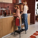 Two in modern kitchen; girl on stool cooking, woman beside, rustic decor.