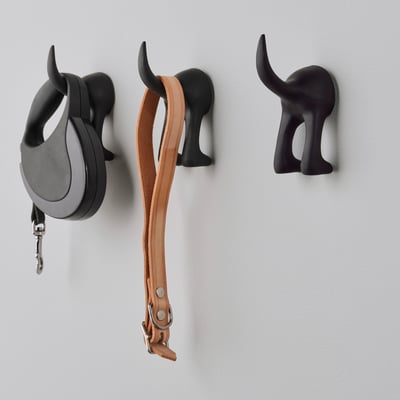 Three black decorative dog head hooks on a wall, one holding a black leash, another a brown leather belt.
