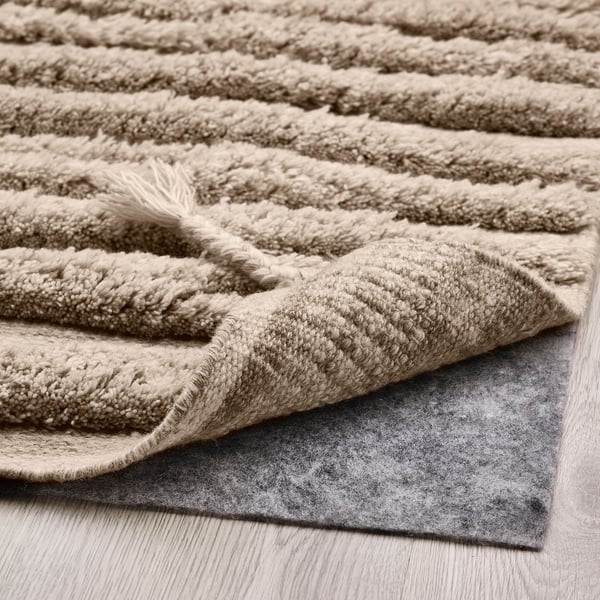 Beige shaggy rug with textured wave pattern, showing thick wool pile and non-slip pad underneath.