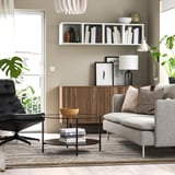 Modern living room with BANKKONTOR rug, gray sofa, coffee table, black chair, wood storage, and plants. Rugs size complements furniture.