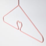A pastel pink hanger with a heart-shaped hook, designed for childrens clothes, anti-slip surfaces and durable steel construction.