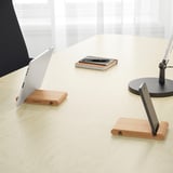 A wooden stand holding a laptop and a tablet upright on a desk. The table is also holding a notepad, pens, and a monitor.