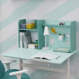 A kids adjustable desk with a tiltable top and shelves. Includes a lamp, books, and storage bins.