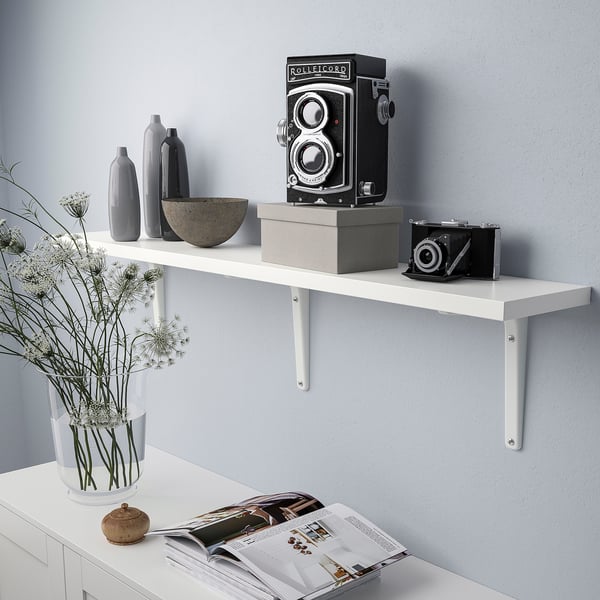 White wall shelf displays cameras and vases. Held by metal brackets.