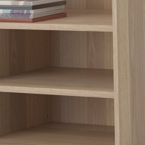 Wooden bookshelf with three empty shelves and a stack of books on top. The shelves are adjustable.