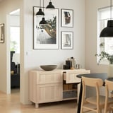 Minimalist dining area with wood storage, adjustable shelves, and coffee setup under art and lights.