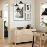Modern kitchen with wooden sideboard featuring drawers & adjustable shelves, against wall with art and lights.