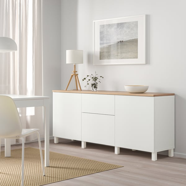 Bright room with white BESTÅ sideboard, wooden top. Displaying lamp, vase, bowl. Art above. Light-colored floor and curtain.