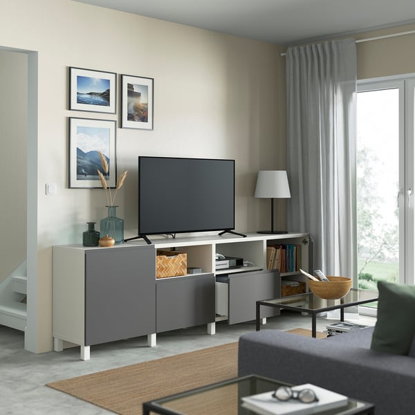 Modern living room with BESTÅ tv bench, adjustable shelves, cable management, flat-screen tv, art, gray curtains, black coffee table, bowl, books.