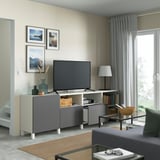 Modern living room with BESTÅ tv bench, adjustable shelves, cable management, flat-screen tv, art, gray curtains, black coffee table, bowl, books.